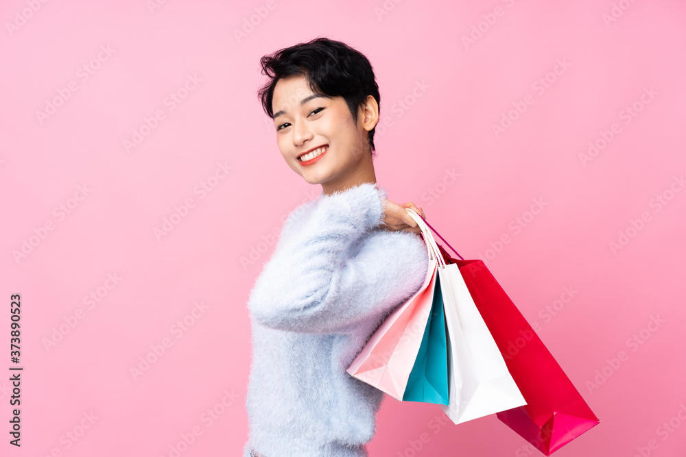 Young Asian girl over isolated pink background holding shopping bags and smiling Young Asian girl over isolated pink background holding shopping bags and smiling