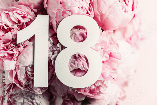 Creative layout. Peony flowers, digit eighteen. Birthday greeting card with inscription 18. Anniversary concept. Top view. Copy space. Stylish white numeral on flower background. Numerical digit
