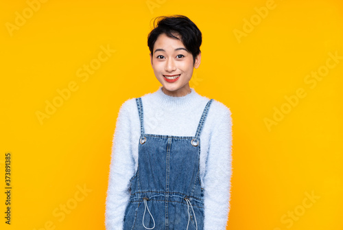 Young Asian girl in overalls over isolated yellow background with surprise facial expression