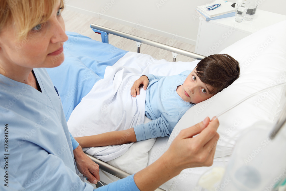 Up view of nurse checking the drip with sick child lying in bed next to her in hospital room Up view of nurse checking the drip with sick child lying in bed next to her in hospital room