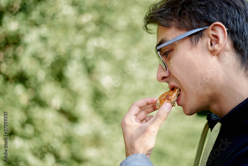 Side view of a man bites appetizing kebab or meat sausage in a park outdoors. Close up with copy space
