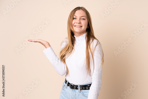 Teenager Ukrainian girl isolated on beige background holding copyspace imaginary on the palm to insert an ad