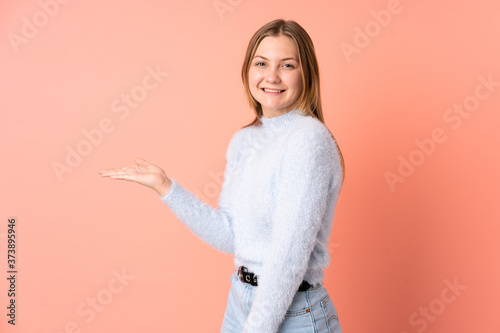 Teenager Ukrainian girl isolated on pink background presenting an idea while looking smiling towards