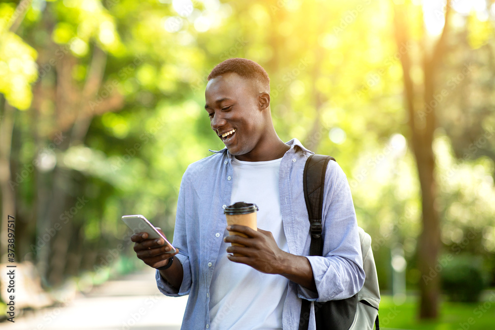 Joyful black man with takeaway coffee using smartphone at city park Joyful black man with takeaway coffee using smartphone at city park