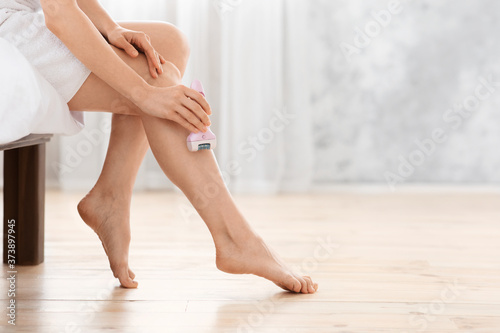 Closeup of woman using epilator for her legs at home photo