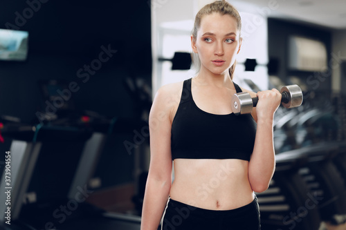 Young brunette sporty woman exercising with dumbbell in a gym