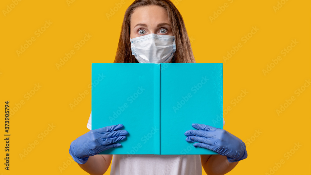 School reopen. Quarantine class. Scared female student in protecting face mask gloves holding open blue book isolated on bright yellow copy space. COVID-19 outbreak. Hygiene measures. Safe education. - obrazy, fototapety, plakaty 
