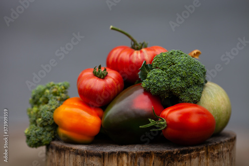 Bright colorful vegetables on a grey concrete background. Fresh organic vegetables  broccoli  tomatoes  pumpkin   peppers  from the garden on a wooden stump. Autumn concept  thanksgiving day  harvest.