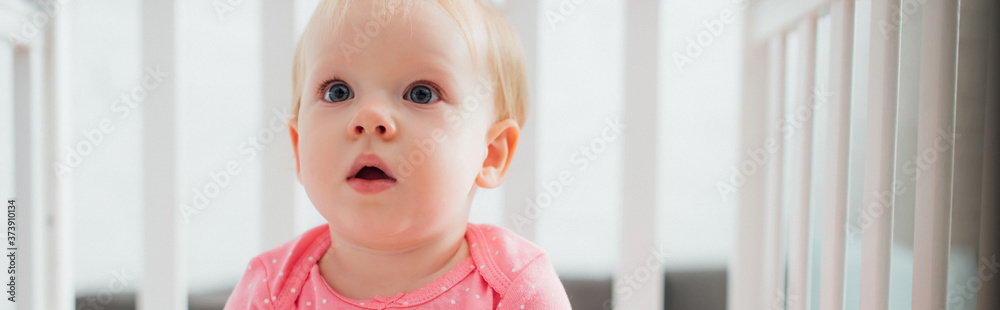 Horizontal crop of excited baby girl looking away in crib Horizontal crop of excited baby girl looking away in crib