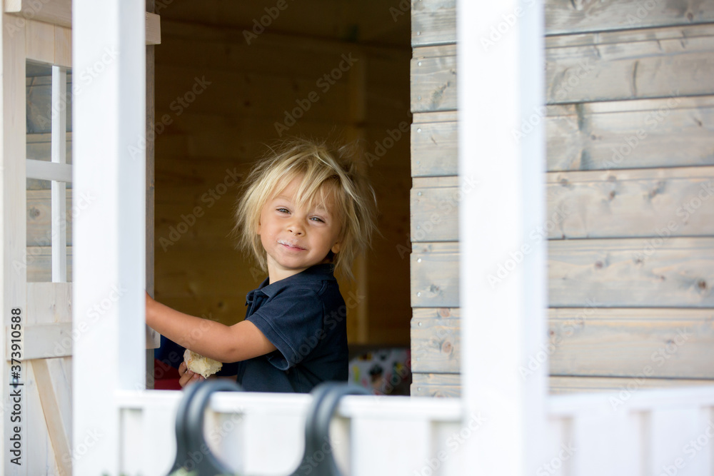 Sweet toddler boy, playing in wooden doll house in garden Sweet toddler boy, playing in wooden doll house in garden