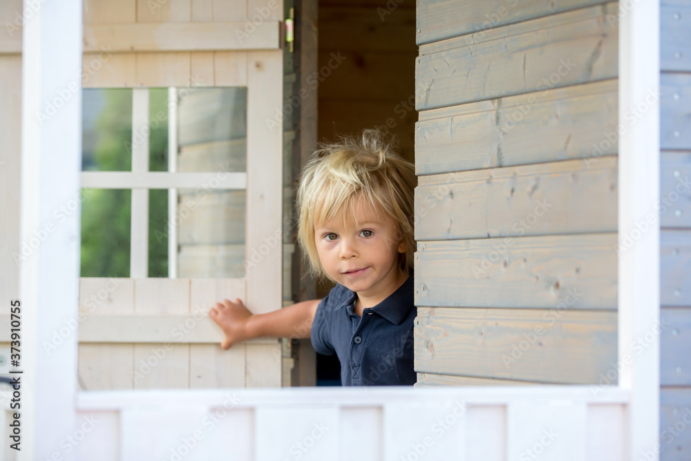Sweet toddler boy, playing in wooden doll house in garden Sweet toddler boy, playing in wooden doll house in garden