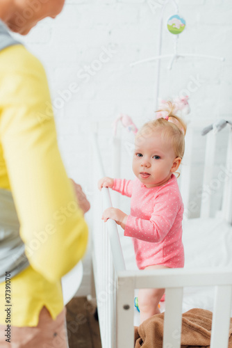 Selective focus of woman standing near baby daughter in crib