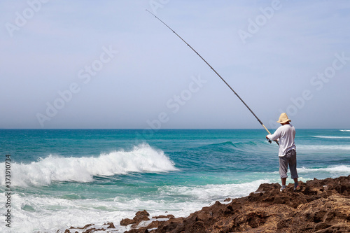 Unknown fisherman on the Atlantic Ocean coast in sunny day.