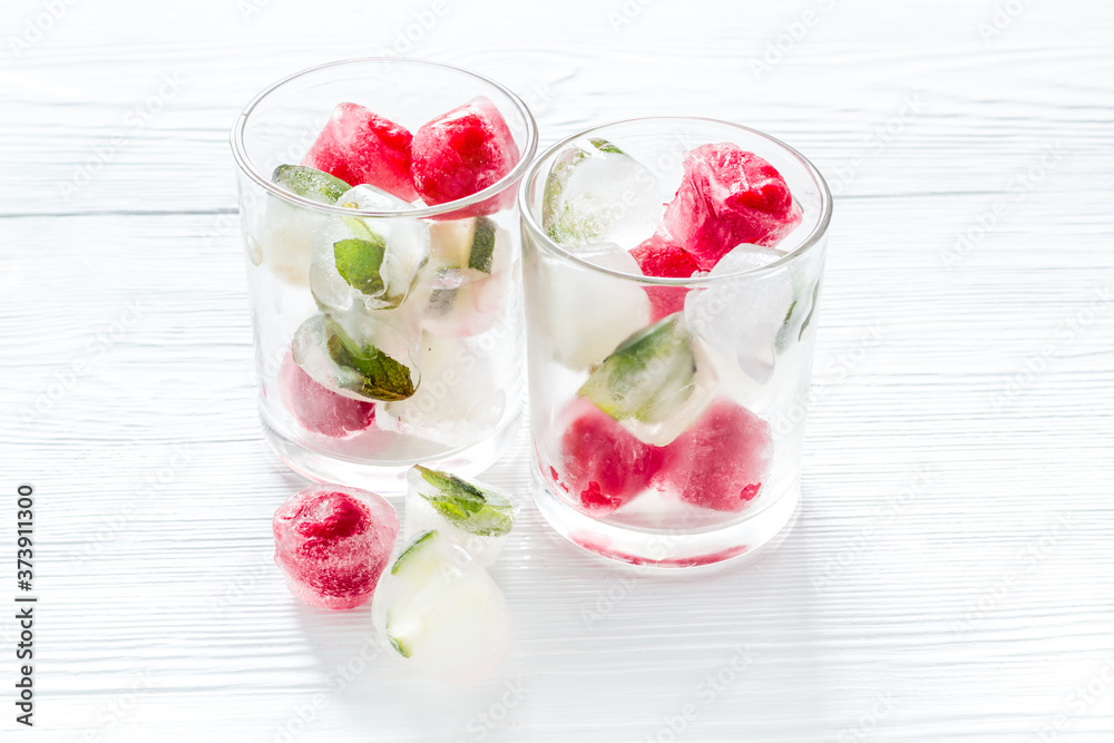 Cocktail glasses with berries in ice cubes on white table Cocktail glasses with berries in ice cubes on white table