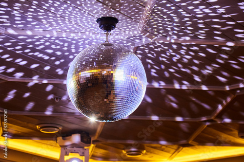 The disco ball reflects white light in a dark room. The concept of a disco, a party, a spinning mirror ball.