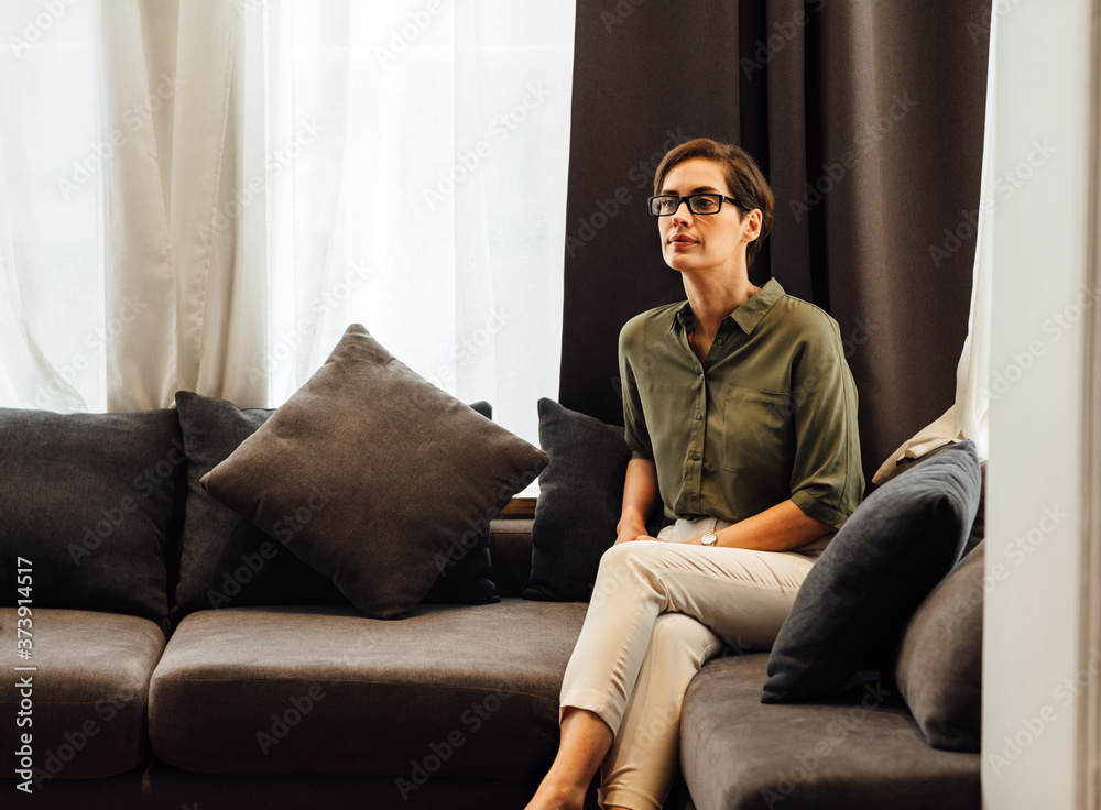 Confident businesswoman sitting in apartment on sofa and looking away