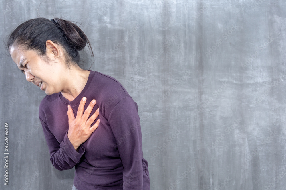 Young Asian woman got chest pain on gray concrete wall for background Young Asian woman got chest pain on gray concrete wall for background