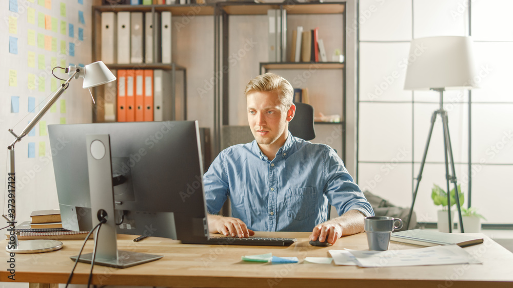 Creative Entrepreneur Sitting at His Desk Works on Desktop Computer in the Stylish Office. Handsome Young Businessman Uses Computer, Does Outsourcing Job, Designs New Apps and Develops Software Creative Entrepreneur Sitting at His Desk Works on Desktop Computer in the Stylish Office. Handsome Young Businessman Uses Computer, Does Outsourcing Job, Designs New Apps and Develops Software