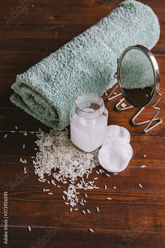 Rice water for skin care. A can of rice water, a handful of rice, a mirror and a folded blue towel on an old wooden table. Cosmetic  product made at home. Vertical frame