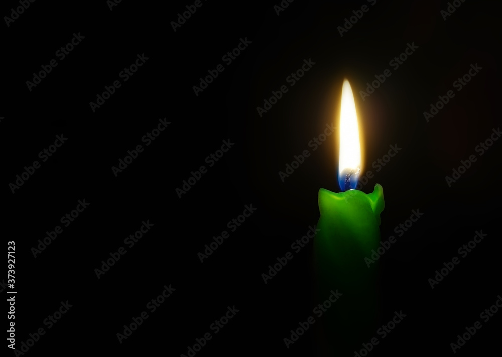 Burning green candle on a black background. Candle flame in the darkness Burning green candle on a black background. Candle flame in the darkness