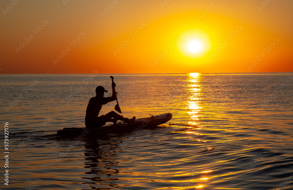 Silhouette of a man floating on a board with an oar. Dawn sun on the sea. Swimming on a supboard. Water active sports. Beautiful landscape. Sunset on the sea. Ocean coast. Copy space. Silhouette of a man floating on a board with an oar. Dawn sun on the sea. Swimming on a supboard. Water active sports. Beautiful landscape. Sunset on the sea. Ocean coast. Copy space.