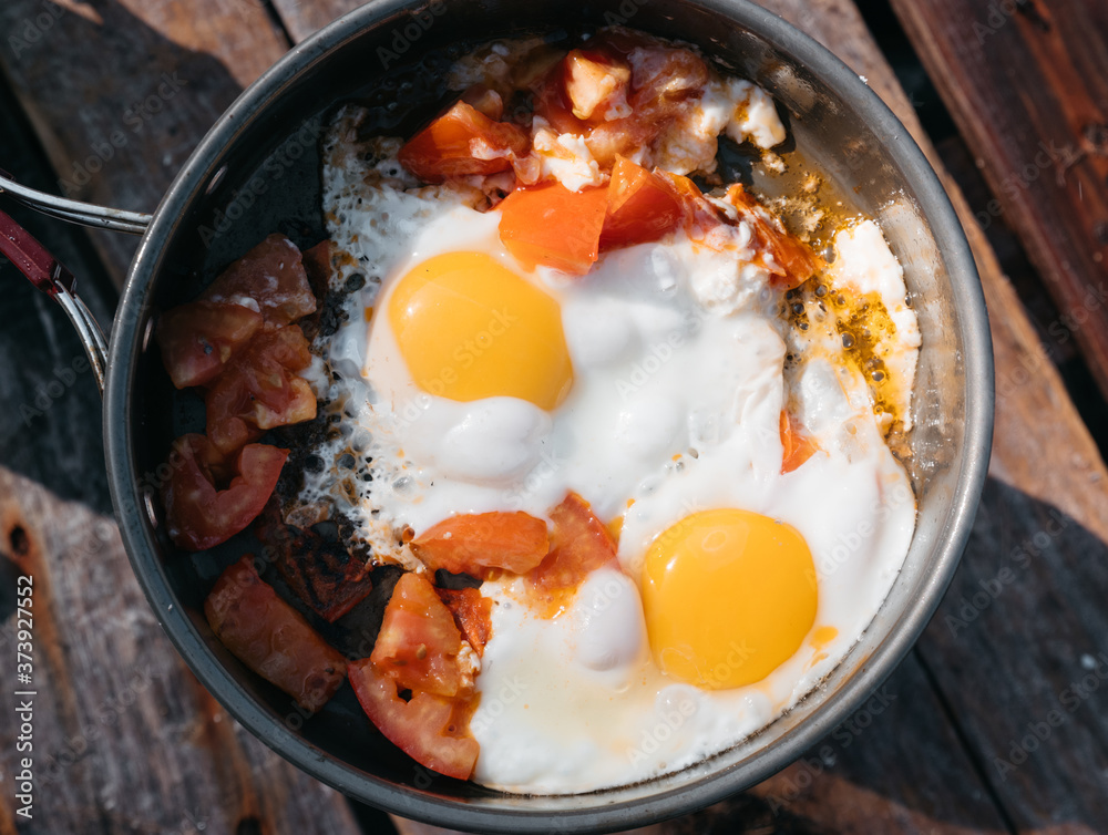 Delicious and healthy Breakfast. Fry eggs on a burner in nature and in the fresh air. Fried eggs with tomatoes close-up view from above. Delicious and healthy Breakfast. Fry eggs on a burner in nature and in the fresh air. Fried eggs with tomatoes close-up view from above.