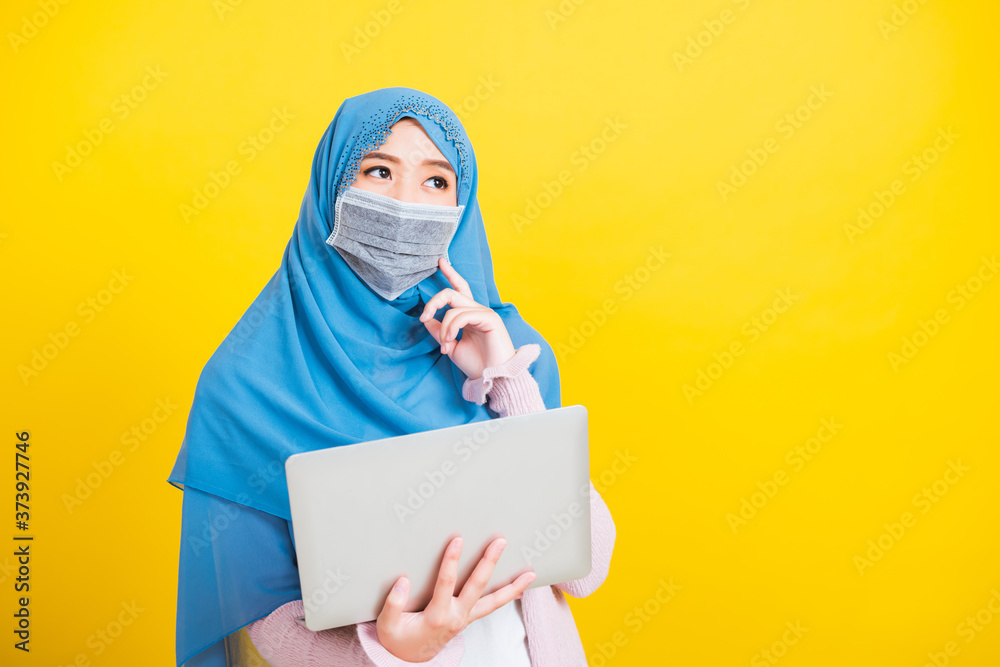 Asian Muslim Arab, Portrait of happy beautiful young woman Islam religious wear veil hijab and face mask protect she quarantines disease coronavirus hold laptop computer and thinking question Asian Muslim Arab, Portrait of happy beautiful young woman Islam religious wear veil hijab and face mask protect she quarantines disease coronavirus hold laptop computer and thinking question