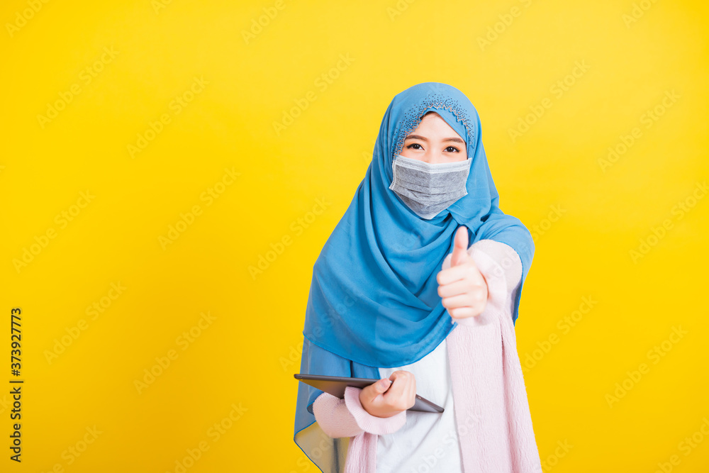Asian Muslim Arab, Portrait of happy beautiful young woman Islam religious wear veil hijab and face mask protect she quarantines disease coronavirus show finger thumb up for good sign isolated yellow Asian Muslim Arab, Portrait of happy beautiful young woman Islam religious wear veil hijab and face mask protect she quarantines disease coronavirus show finger thumb up for good sign isolated yellow