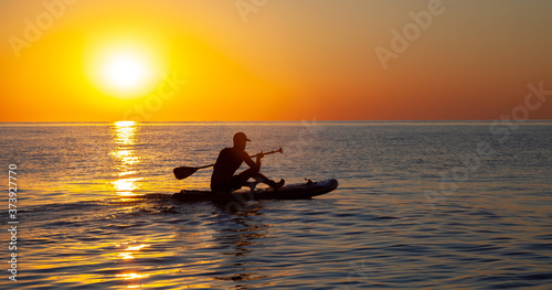Silhouette of a man floating on a board with an oar. Dawn sun on the sea. Swimming on a supboard. Water active sports. Beautiful landscape. Sunset on the sea. Ocean coast. Copy space.