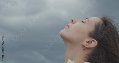 Close up portrait of female face looking up into stormy sky copy text space. Detailed macro side view of woman with closed eyes on nature rainy background slow motion. Facial care cosmetics products