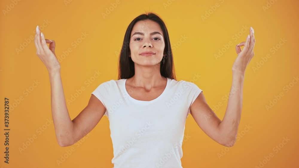 Woman taking deep breaths, closes eyes, showing gyan mudra hands gesture and meditating. Posing on orange background Woman taking deep breaths, closes eyes, showing gyan mudra hands gesture and meditating. Posing on orange background