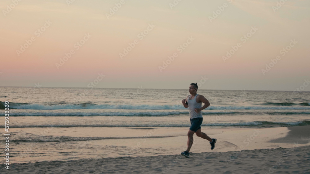 Athletic Man is Jogging on Beach and Running along Sea Coast at Sunset Athletic Man is Jogging on Beach and Running along Sea Coast at Sunset