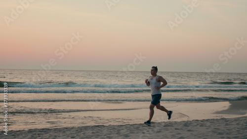 Athletic Man is Jogging on Beach and Running along Sea Coast at Sunset