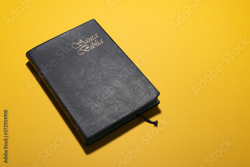 Santa Biblia (Holy Bible in spanish) over mustard yellow desk. Copy space for adding text, design, logos, timetable, wedding, communion schedule, masses, catechism, catechesis