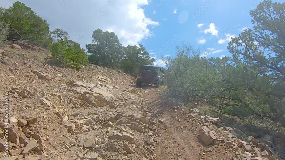 POV following an all terrain vehicle while driving on a rocky off-road trail down a mountain in Colorado on a cloudy day