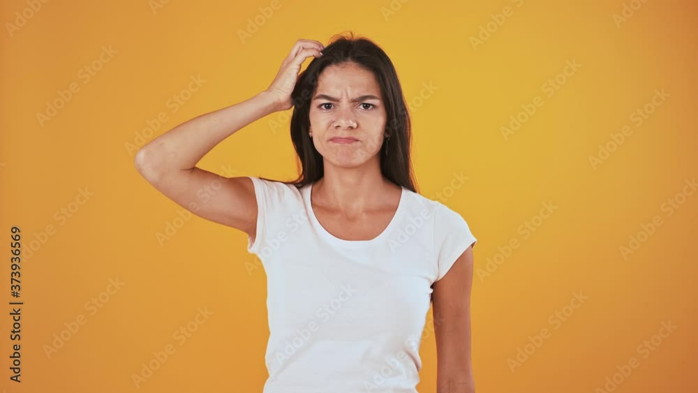 Thoughtful and disappointed woman is scratching her head, shrugging shoulders over orange background Thoughtful and disappointed woman is scratching her head, shrugging shoulders over orange background