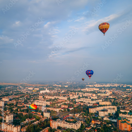 Colorful hot air balloons flying over small european city at summer sunset