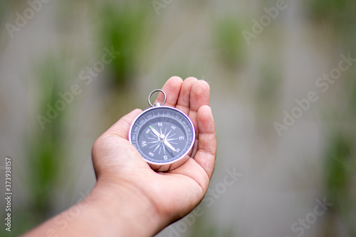 Hand holding a compass with natural blurred green background.. - travel and transportation concept.