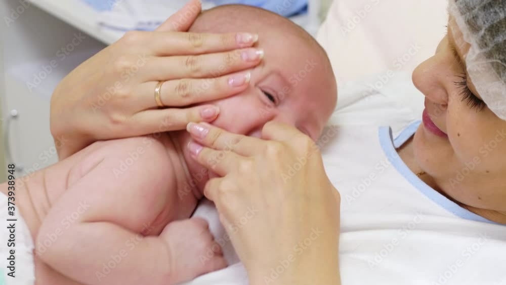 Close up shot of loving mother trying to clean nose of newborn baby with cotton swab and comforting crying child in hospital ward