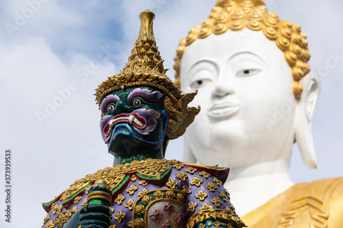 face of green giant statue contrast with great white Buddha at Wat Phra That Doi Kham, Chiang Mai, Thailand
