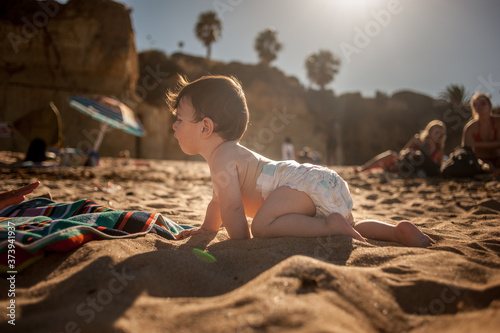 Profile view of a baby boy crawling in the sand in a sunny hot day.