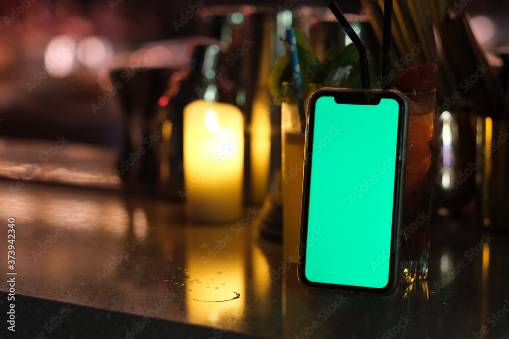 close up green screen smart phone on bar counter at night. defocused candle light and cocktail close up green screen smart phone on bar counter at night. defocused candle light and cocktail