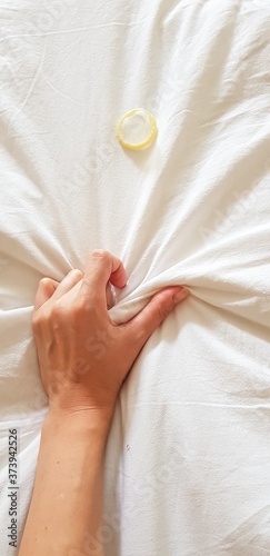 Close up sexy woman hand pulling and squeezing white sheets in ecstasy in bed. Orgasm on white bed. Sex and erotic concept. Condom on a white background. The concept of safe sex and protection from