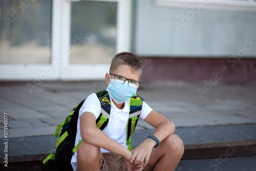 Back to school. Shoolboy in 
glasses wearing mask and backpacks protect and safety from coronavirus. Child going school after pandemic over. Standing near school. students are ready for new year. photo