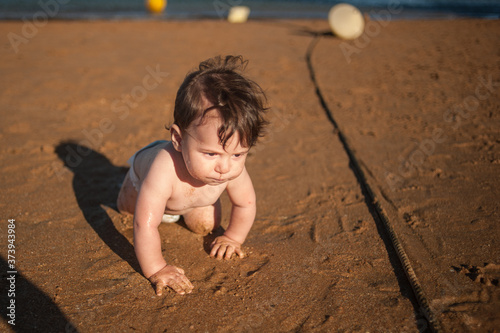 front view of a baby boy playing in the sand in a sunny day. He is crawling. Great Copy space