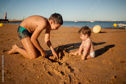 Profile view view of an older boy playing at the beach with his little toddler brother.Great copy space