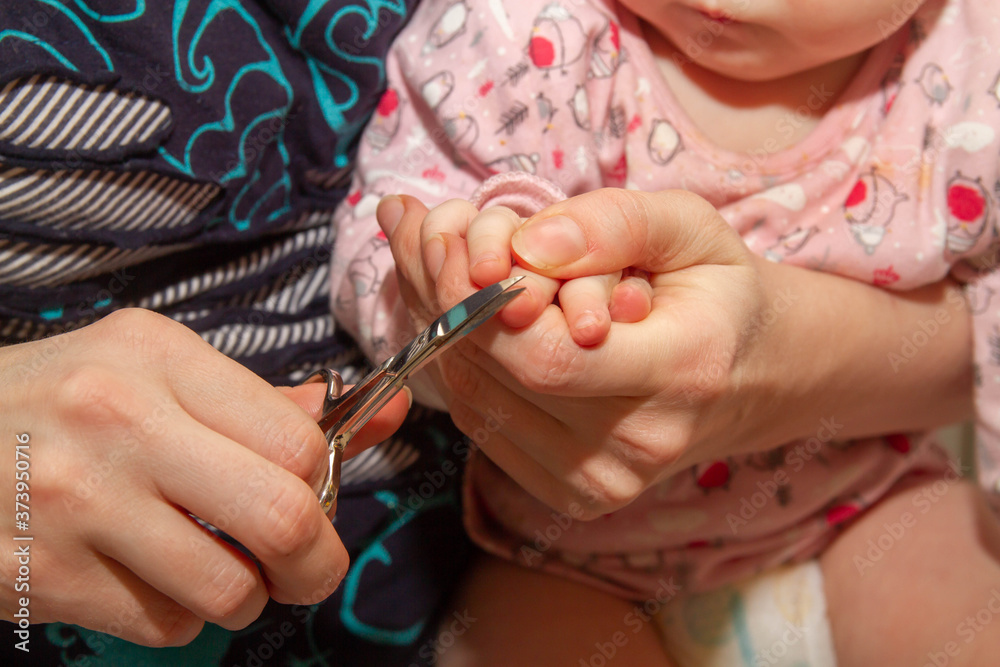A mother cuts her nails with scissors for a small child.