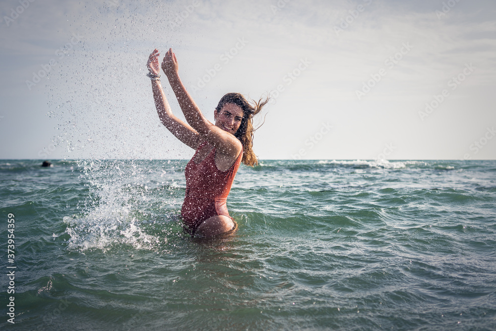 Beautiful young European woman with an orange swimsuit splashing water at the sea in Cádiz