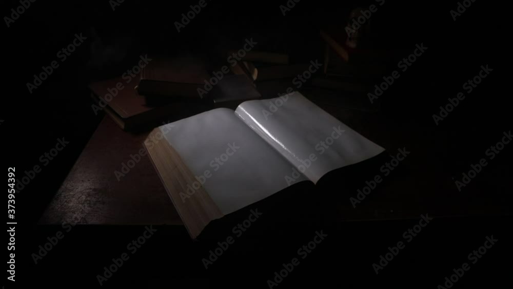 A stack of old books. Vintage book on wooden table. Magic lightning around a glowing book in the room of darkness. Selective focus