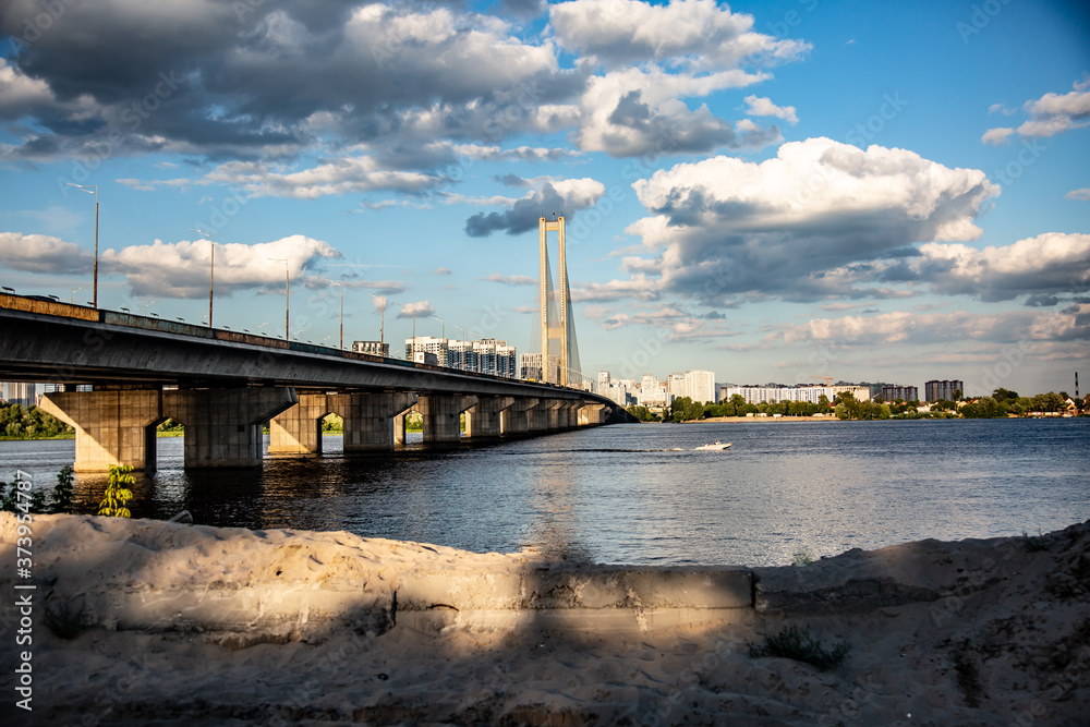 South bridge in Kyiv Ukraine. Bottom view from the right sandy bank of the bridge, the Dnieper and the left bank. Sunny day and sky with clouds. Horizontal orientation. High quality photo